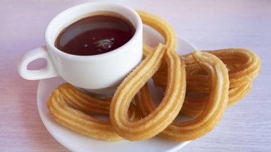 Churros con çikolatalı caliente, geleneksel bir İspanyol sokak yemeği, bir fincan kalın sıcak çikolata içeceği ve kıtır kıtır, uzun ve kıvırcık hamur tatlısı içeren tatlı bir ikram.