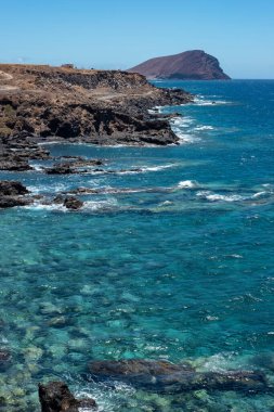Los Abrigos köyü ile La Tejita plajı arasındaki kıyı şeridi manzarasında doğal su havuzları, volkanik kayalar ve Tenerife, Kanarya Adaları, İspanya 'daki Montana Roja' nın vahşi manzarası görülüyor.