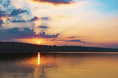 Bulutlar ve gökyüzü kırmızı, mavi, turuncu ve mavi bir göl üzerinde günbatımı.