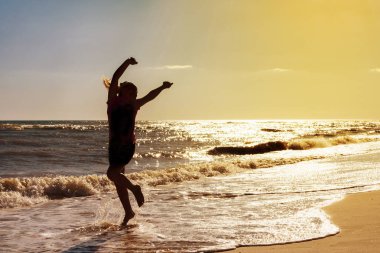 Dans ve deniz kıyısında güneşin arka planda üzerinde sıçrayan kız