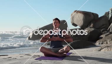 Genç adam arka plan taşlara birlikte kumsala yoga yaparken