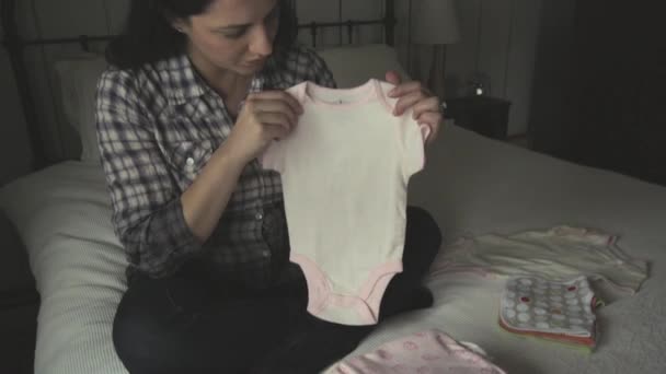 妊娠中の母親がベッドに座って 赤ちゃんの服を折りたたむ — ストック動画