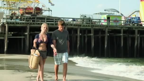 代のカップルがビーチで手をつないでを歩く — ストック動画