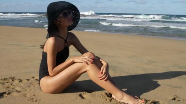 サングラスと Sunhat のビーチに座っている若い女性 — ストック動画