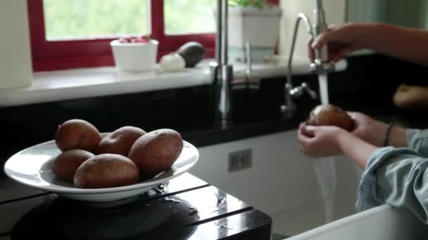若い女性と息子台所のシンクでジャガイモを洗う — ストック動画