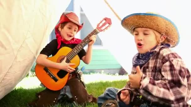 Dva kluci převlečení za kovboje zpívající a hrající na kytaru