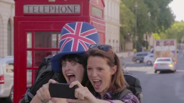 電話ボックスの横でセルフを撮る2人の女性観光客 — ストック動画