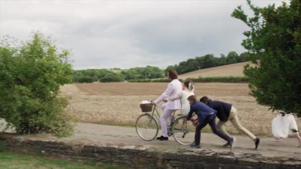 田舎の風景の中で新婚夫婦と自転車を押す子供たち — ストック動画