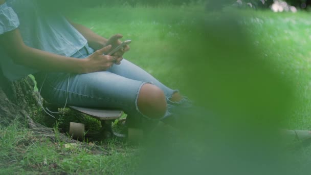 Γυναίκα Κάθεται Στο Skateboard Κατά Δέντρο Και Χρήση Smartphone — Αρχείο Βίντεο