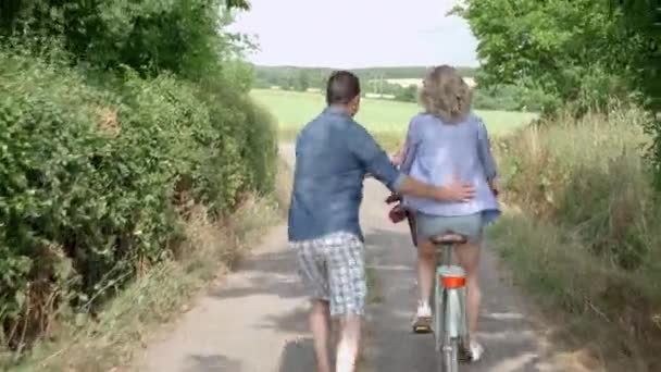 Uomo Che Assiste Donna Mentre Pedala Sulla Strada Sterrata — Video Stock