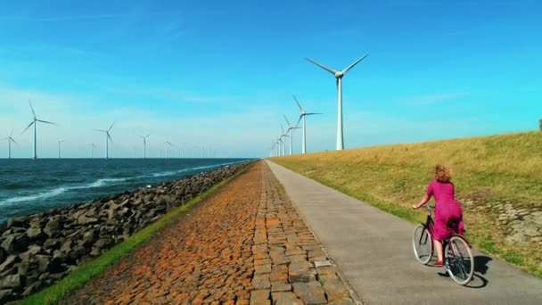 女孩骑自行车沿风力涡轮机在海上和陆地上 乌尔克 弗莱沃兰 — 图库视频影像