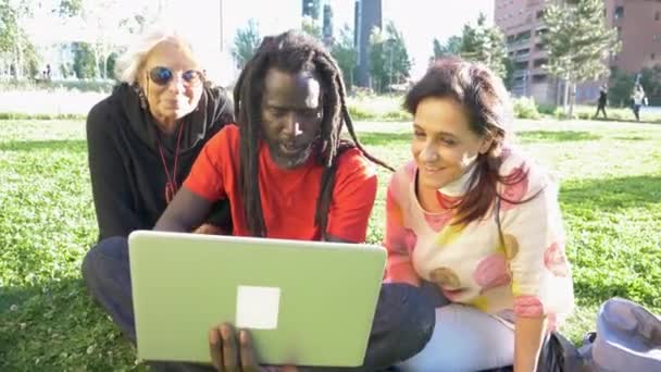 Две Женщины Мужчина Дредами Сидят Лавочке Парке Смотрят Ноутбук — стоковое видео