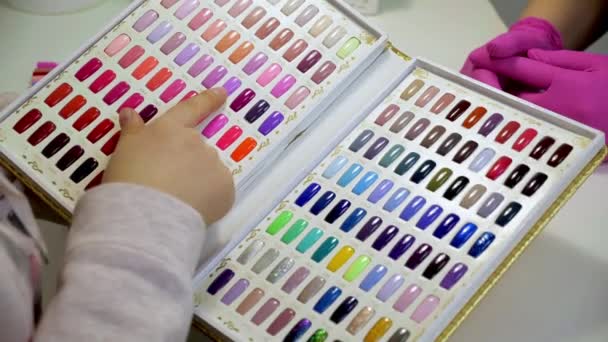 Femme choisit une couleur pour peindre des ongles dans un salon de beauté. Une collection de testeurs de vernis à ongles en différentes couleurs . — Video