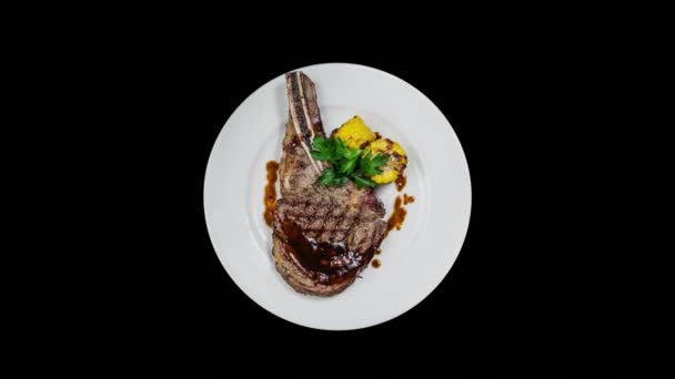 Rib-eye steak with corn rotating on a white plate. Top view, Isolated on the black background. — Stock Video