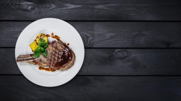 Rib-Eye-Steak mit Mais rotiert auf einem weißen Teller. Draufsicht auf schwarzem Holzhintergrund. Kopierraum für Ihren Text. — Stockvideo
