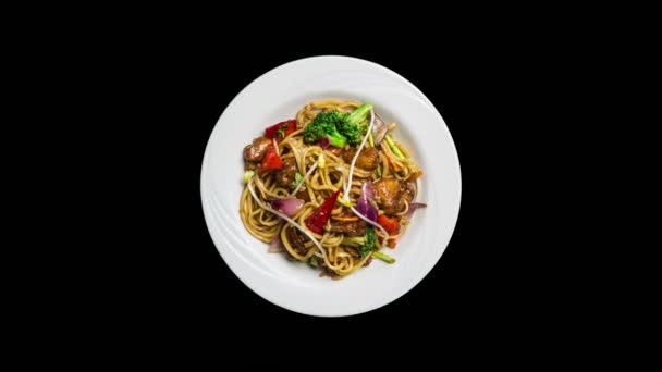 Rotating udon stir fry noodles with meat or chicken and vegetables isolated on ablack background. Top view — Stock Video