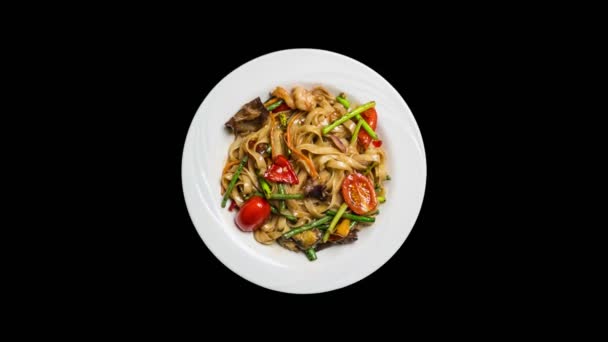 Εκ περιτροπής αναδεύεται τηγανητά noodles udon με θαλασσινά και λαχανικά που απομονώνονται σε ablack φόντο. Το top view — Αρχείο Βίντεο