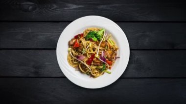 Udon stir fry erişte et ya da tavuk ve sebze siyah ahşap zemin üzerine beyaz bir plaka ile döner. Üstten Görünüm