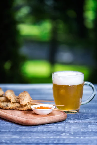 Conjunto de aperitivos de cerveza. Alitas de pollo en palitos y jarra de cerveza. En la tabla de cortar y fondo verde de verano — Foto de Stock