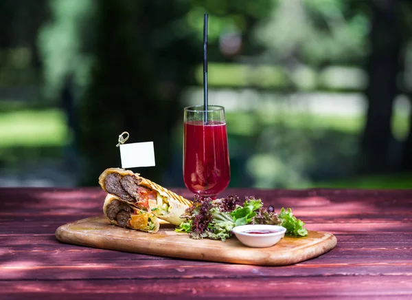 Biftek, yeşil salata, sos ve limonata ile sağlıklı shawarma sandviç. Ahşap tahta kesme ve yeşil yaz arka plan üzerinde.