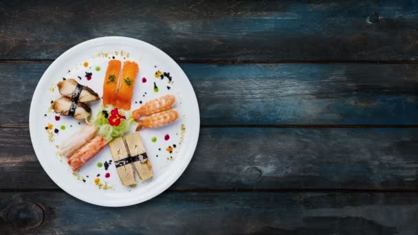 Set de sashimi giratorio en un plato redondo blanco, decorado con flores pequeñas, comida japonesa, vista superior. Fondo de madera con el espacio de copia para su texto — Vídeo de stock