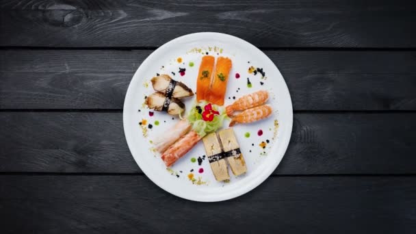 Rotierendes Sashimi-Set auf einem weißen runden Teller, dekoriert mit kleinen Blumen, japanisches Essen, Draufsicht. schwarzer Holzhintergrund — Stockvideo