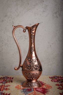El yapımı desenleri ve ulusal desen ve baskılar, gri bir duvara bir halı bir masada duran süs eşyaları ile eski bir bakır sürahi.