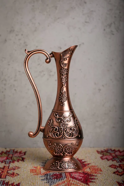 El yapımı desenleri ve ulusal desen ve baskılar, gri bir duvara bir halı bir masada duran süs eşyaları ile eski bir bakır sürahi.