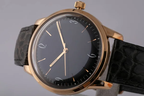 黒革のストラップは、ブラック ダイヤル、黄金ボディ、時計回りに黄金と灰色の背景に分離された数字でメンズ腕時計. — ストック写真