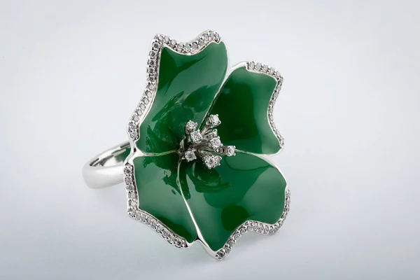 Silver flower-shaped ring from green stone  and diamonds in the middle of flower, isolated on white background