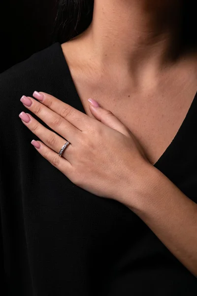 Womens silver ring with diamonds on finger, on  a black background.