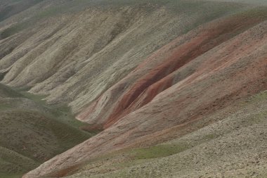 Tepeler ve dağlar gökyüzüne karşı yamaçlarda kırmızı çizgiler ile bitki örtüsü ile kaplı.