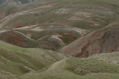 Tepeler ve dağlar gökyüzüne karşı yamaçlarda kırmızı çizgiler ile bitki örtüsü ile kaplı.