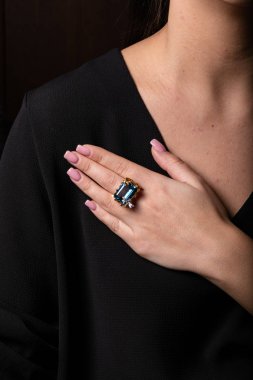 Kadınların altın yüzüğü. Elmaslar ve mavi büyük taş. Parmağın ortasında kare şeklinde, siyah bir zemin üzerinde..  