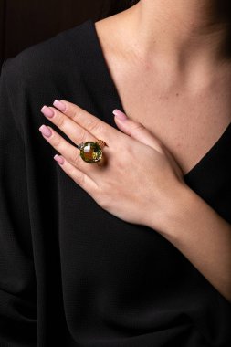 Kadınların altın yüzüğü, elmaslar ve orta parmağında yeşil büyük bir taş, siyah bir arka planda..