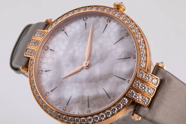 Female gold watch with a grey dial, golden clockwise, framing of the stones, with a brown cloth strap