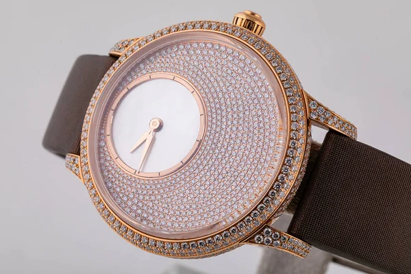 Reloj de pulsera de oro femenino con esfera de piedras, dorado en el sentido de las agujas del reloj, con correa de tela marrón sobre fondo blanco . — Foto de Stock