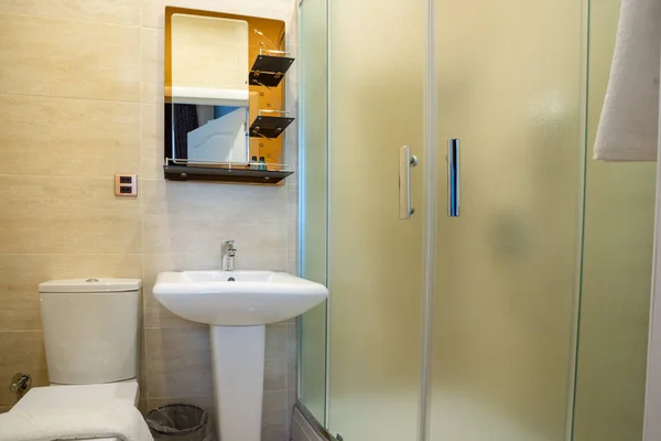 Camlı duş, lavabo üzerinde ayna, havlu ve tuvalet ile bej banyo.