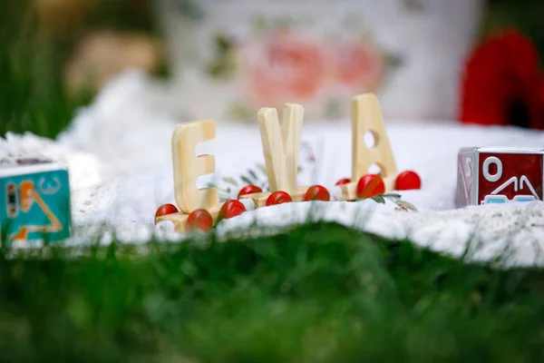 Wooden letters of the name Eve standing on a white tablecloth, on the green grass.