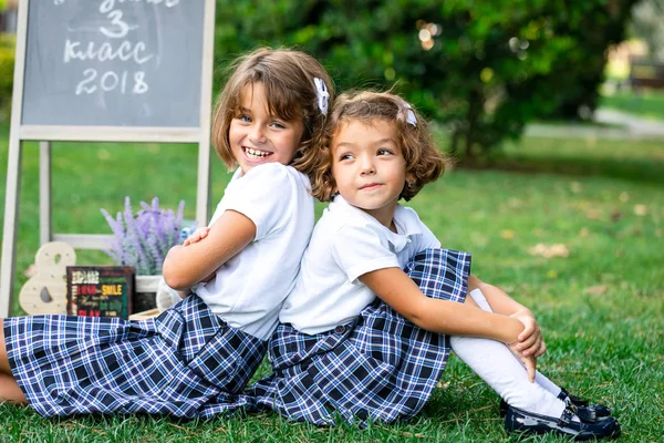 Meninas em camisetas brancas e saias xadrez sentado de volta para trás . Imagem De Stock