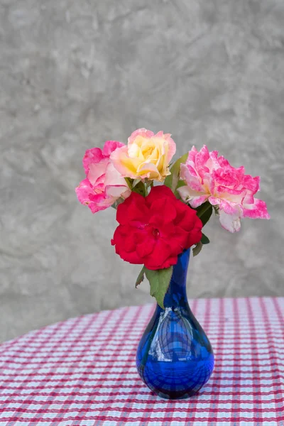 Beautiful red and pink roses in blue vase on red and white checkered table background,still life
