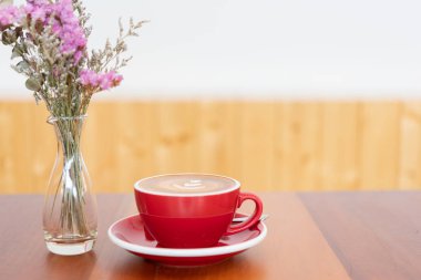 Ahşap masa ve çiçek vazo üzerinde latte sanat ile Kırmızı sıcak kahve fincanı