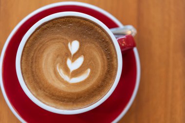 Ahşap arka plan üzerinde kırmızı fincan latte sanat ile sıcak kahve fincanı, fla