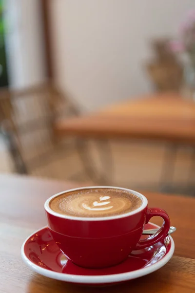 Šálek horkého kávy s Latte art v červeném šálku na dřevěného stolku v kavárně — Stock fotografie