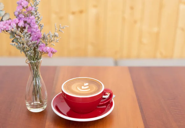 Horká káva s červeným šálkem s Latte na dřevěné stolové a květové váze — Stock fotografie