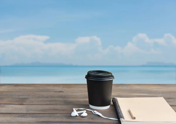 Filiżanka do kawy, ucho telefon i notebook Ion drewniany blat z letnim morzem — Zdjęcie stockowe