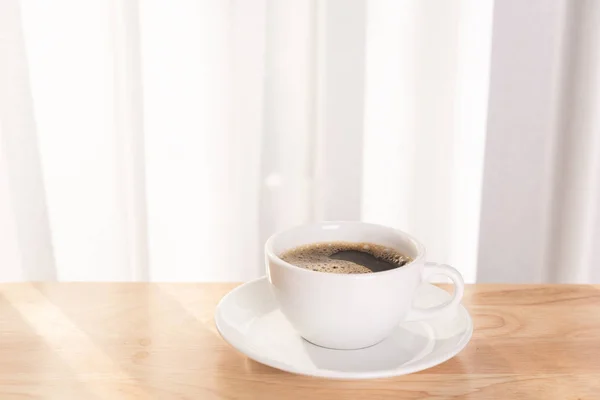Bílý šálek kávy na dřevěné kancelářské desce s ranním slunečním zářením — Stock fotografie