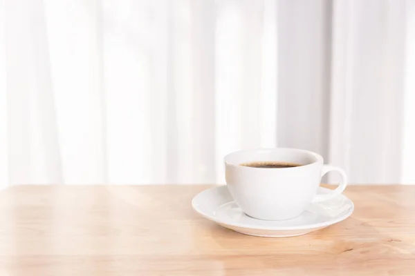 Biała filiżanka kawy na drewnianym biurku z porannym światłem słonecznym — Zdjęcie stockowe