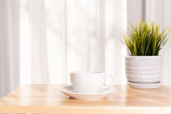 Copo de café branco e vaso de plantas na mesa de escritório de madeira com morni — Fotografia de Stock