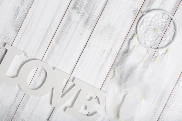 White dream catcher and love text on wooden background, flat lay — стоковое фото